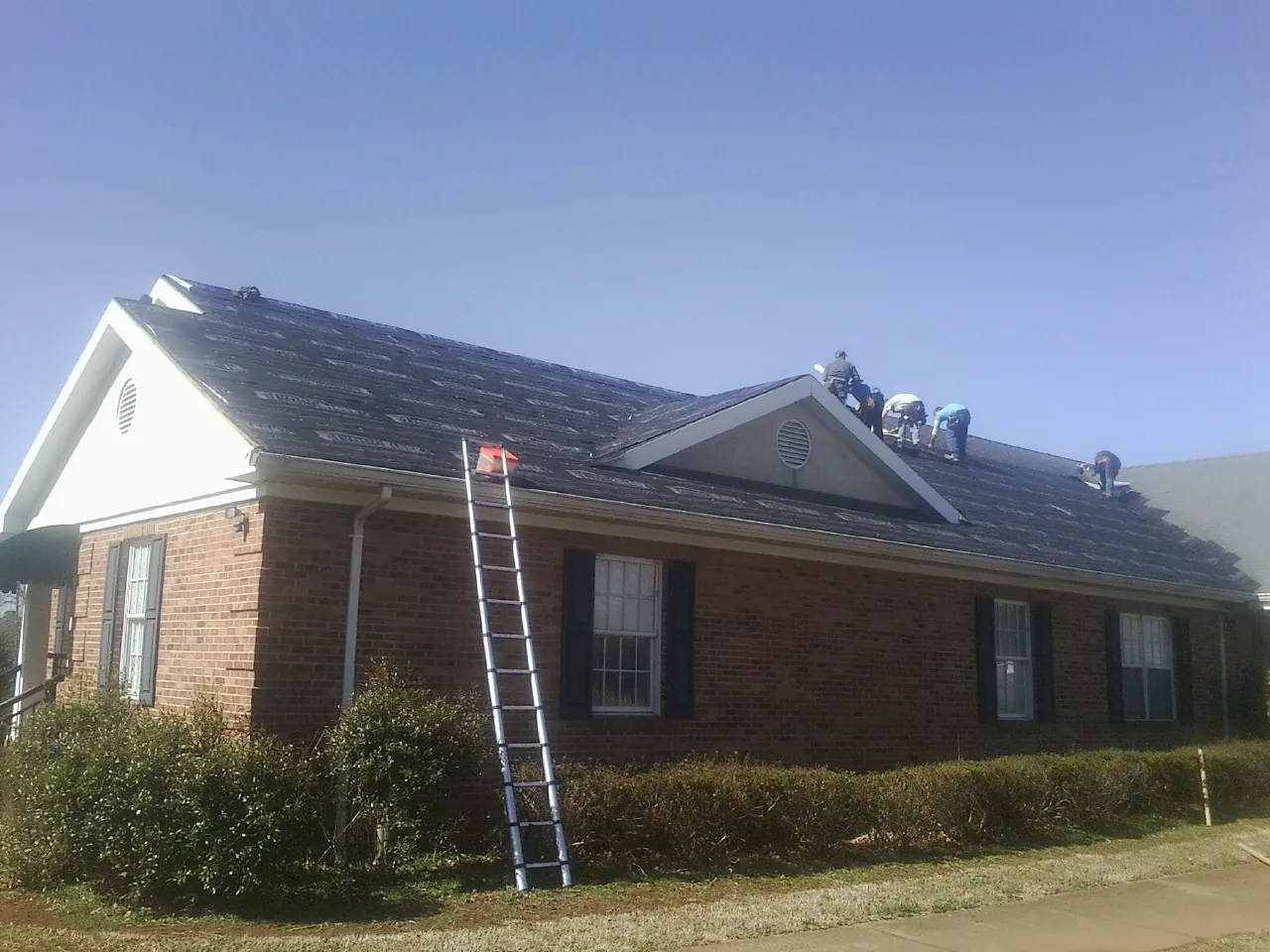 Crew tearing shingles off a brick ranch roof with a ladder set — Emergency Roof Repair work by our crew in Arkville