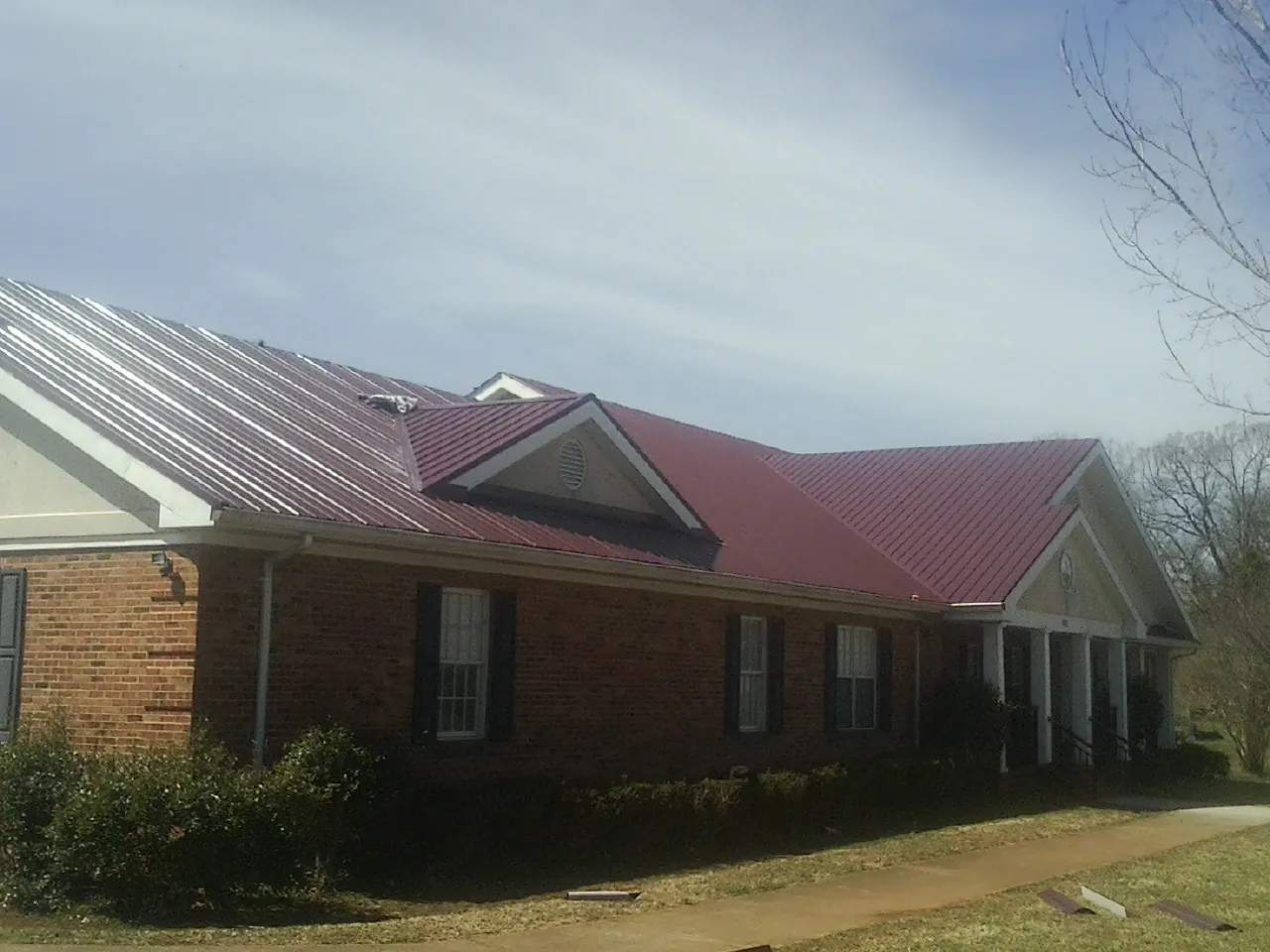 Red metal roof with gabled entries on a long brick building, from a Hail Damage Roof Repair job in Arkville