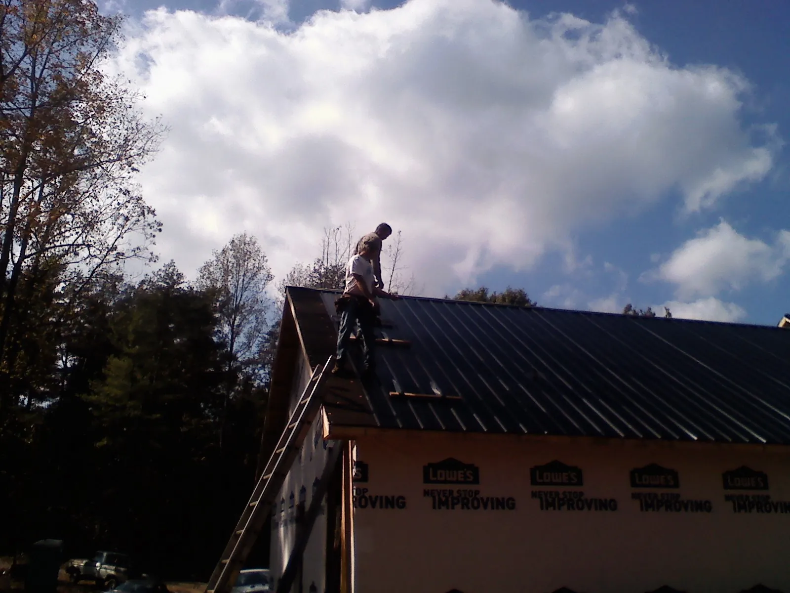 Roofer fastening dark metal panels high against a cloudy sky, from a Roof Inspection job in Arkville