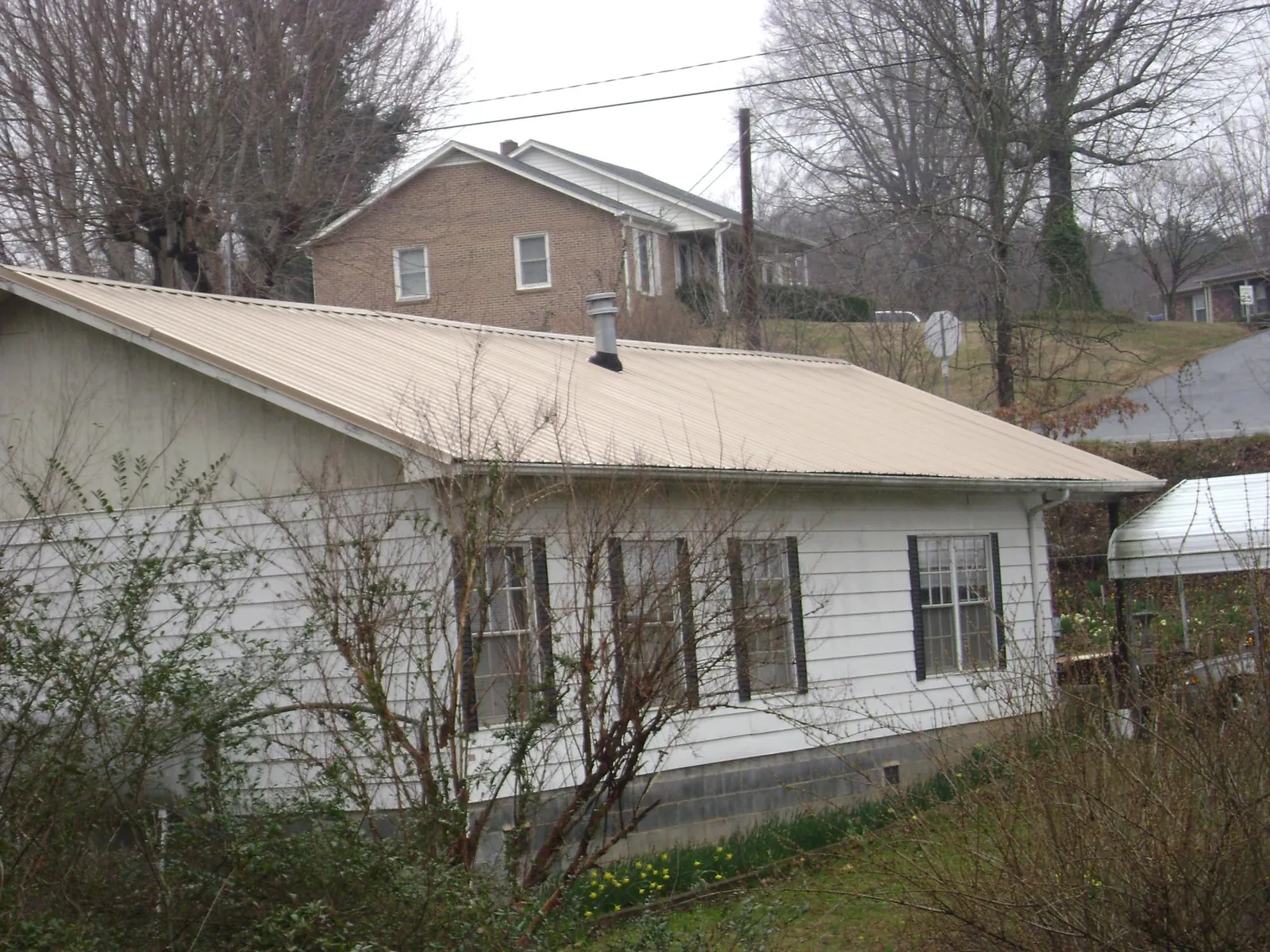 Tan metal roof on a white sided house set into a hillside — Commercial Roofing by Roofing Brothers in Arkville